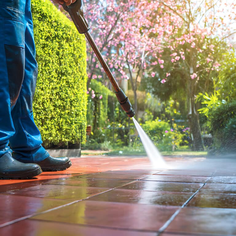 Man in Blue Overalls Pressure Washing Red Tiled Patio with Flowering Tree